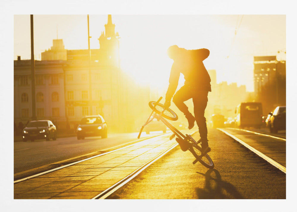 A silhouetted BMX rider performs a trick on a city street during a brilliant golden sunset, with the sun flaring behind them and casting long shadows on the tram tracks. Decor