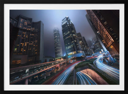 A dynamic, low-angle, long-exposure shot of a modern city at night. Towering skyscrapers with illuminated windows pierce through a foggy, dark blue sky. Below, curving highways are filled with the vibrant red and white light trails of moving traffic. Print
