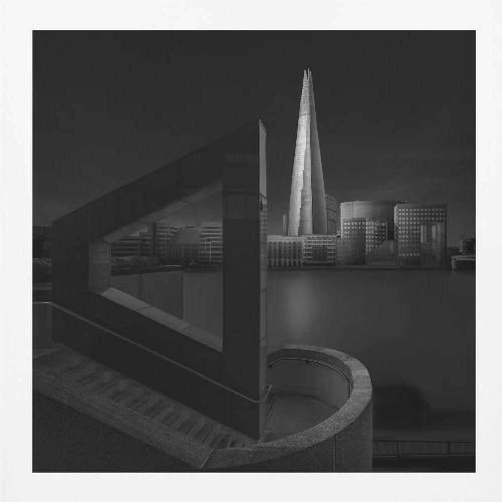A dramatic black and white architectural photograph of the London skyline at night. The illuminated Shard skyscraper stands tall in the background across a dark river. The foreground features strong geometric shapes, including a large triangular structure and a curved concrete staircase, creating a layered and modern composition. Print