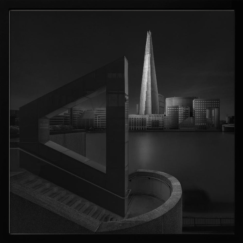A dramatic black and white architectural photograph of the London skyline at night. The illuminated Shard skyscraper stands tall in the background across a dark river. The foreground features strong geometric shapes, including a large triangular structure and a curved concrete staircase, creating a layered and modern composition. Print
