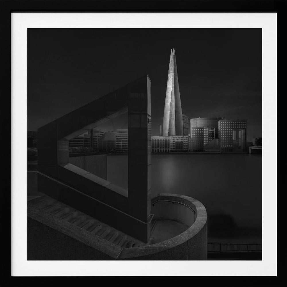 A dramatic black and white architectural photograph of the London skyline at night. The illuminated Shard skyscraper stands tall in the background across a dark river. The foreground features strong geometric shapes, including a large triangular structure and a curved concrete staircase, creating a layered and modern composition. Print