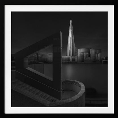 A dramatic black and white architectural photograph of the London skyline at night. The illuminated Shard skyscraper stands tall in the background across a dark river. The foreground features strong geometric shapes, including a large triangular structure and a curved concrete staircase, creating a layered and modern composition. Print