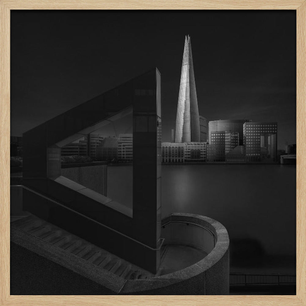 A dramatic black and white architectural photograph of the London skyline at night. The illuminated Shard skyscraper stands tall in the background across a dark river. The foreground features strong geometric shapes, including a large triangular structure and a curved concrete staircase, creating a layered and modern composition. Print