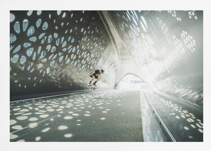 A skateboarder is captured mid-air performing a trick inside a futuristic, metallic tunnel with patterned cutouts that cast dappled light and shadows across the scene, all enclosed within a silver frame. Artwork