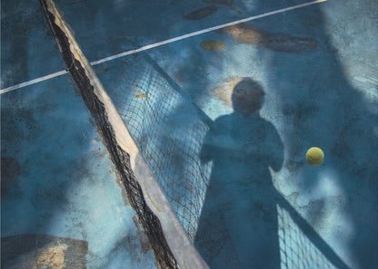 An artistic, high-angle shot of a weathered blue tennis court. The shadow of a tennis player holding a racket is cast across the court, with a yellow tennis ball suspended in mid-air nearby. A tattered tennis net runs diagonally across the frame, all enclosed within a silver border. Wall Art