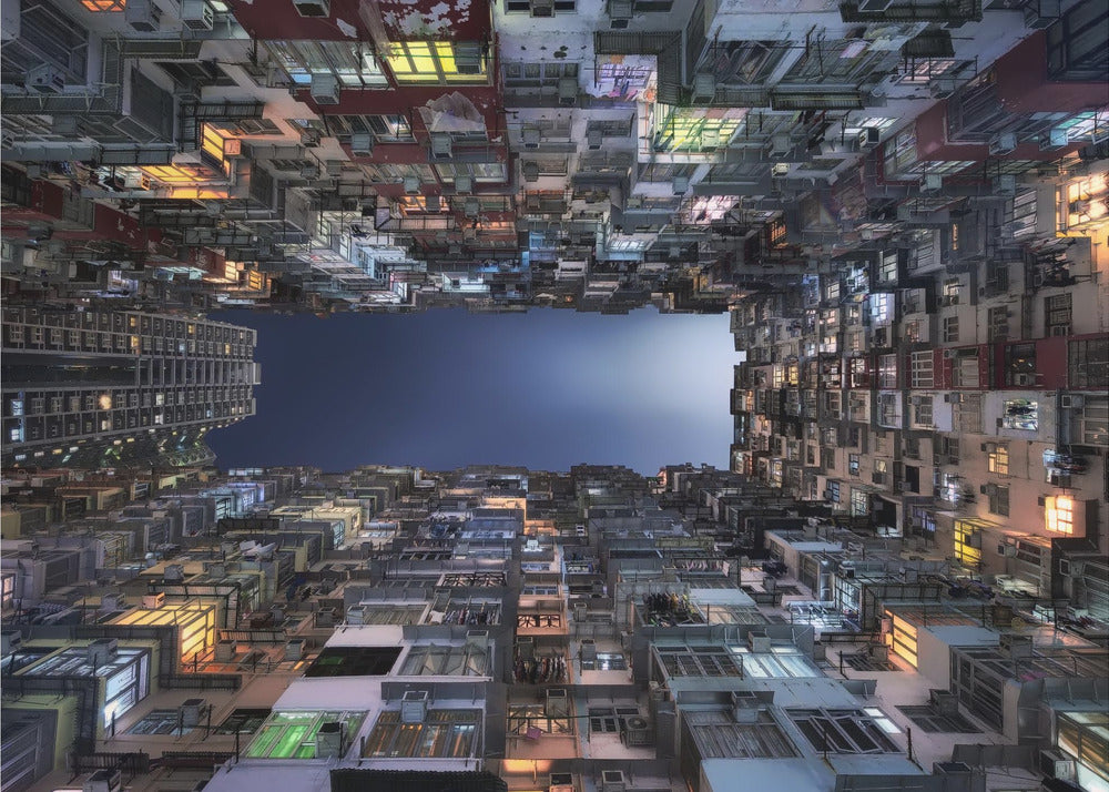 A striking low-angle photograph looking up from a narrow courtyard at the night sky, completely framed by towering, densely packed, and weathered apartment buildings with glowing windows, creating a sense of urban enclosure. Decor