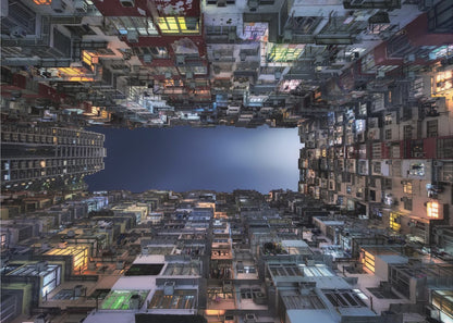A striking low-angle photograph looking up from a narrow courtyard at the night sky, completely framed by towering, densely packed, and weathered apartment buildings with glowing windows, creating a sense of urban enclosure. Decor