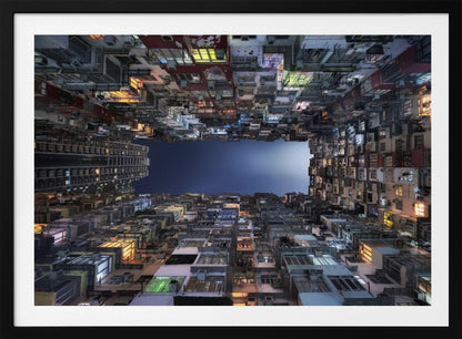 A striking low-angle photograph looking up from a narrow courtyard at the night sky, completely framed by towering, densely packed, and weathered apartment buildings with glowing windows, creating a sense of urban enclosure. Decor