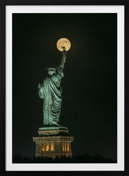A striking night photograph of the Statue of Liberty, where a large, full yellow moon is perfectly aligned behind the torch, creating the illusion that the statue is holding up the moon. Artwork