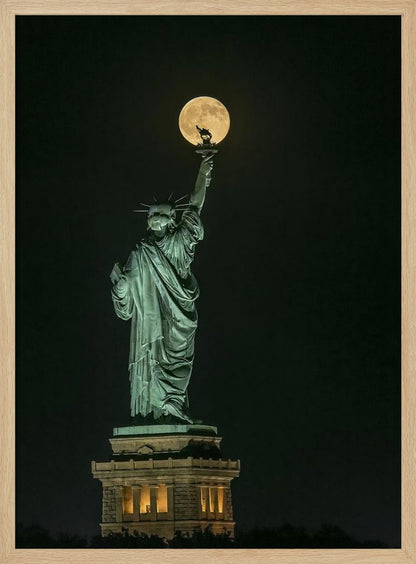 A striking night photograph of the Statue of Liberty, where a large, full yellow moon is perfectly aligned behind the torch, creating the illusion that the statue is holding up the moon. Artwork