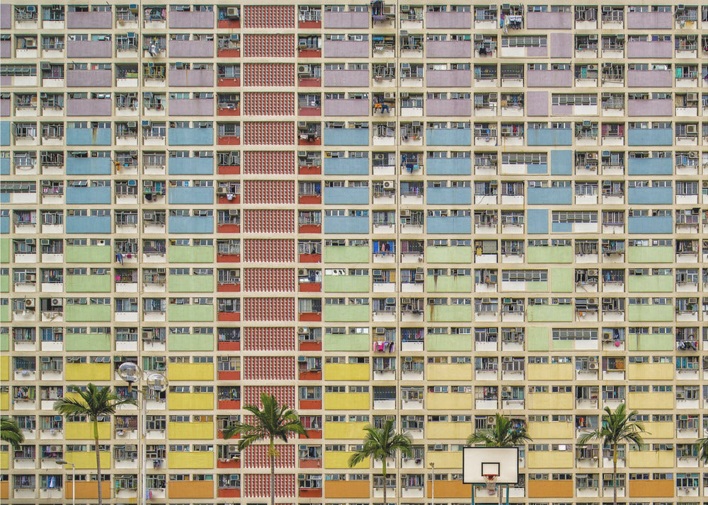 A symmetrical, frontal photograph of the colorful Choi Hung Estate in Hong Kong, featuring a massive grid of apartments with balconies painted in a rainbow of pastel colors including purple, blue, green, yellow, and orange. Palm trees and a basketball court are visible at the base of the building, which is enclosed in a silver frame. Wall Art