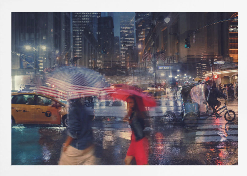An artistic motion-blur photograph of a rainy night on East 42nd Street in New York City. Pedestrians with umbrellas, one with an American flag design and another bright red, cross the wet street as city lights and a yellow taxi reflect on the pavement, creating a vibrant, impressionistic scene within a silver frame. Decor