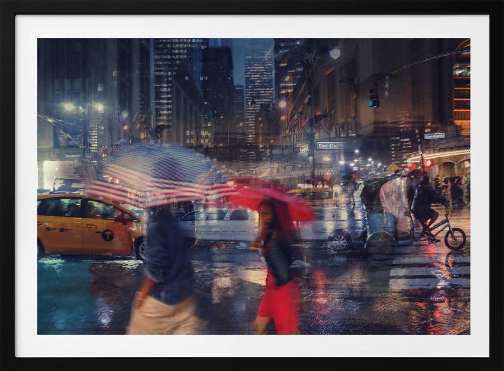 An artistic motion-blur photograph of a rainy night on East 42nd Street in New York City. Pedestrians with umbrellas, one with an American flag design and another bright red, cross the wet street as city lights and a yellow taxi reflect on the pavement, creating a vibrant, impressionistic scene within a silver frame. Decor