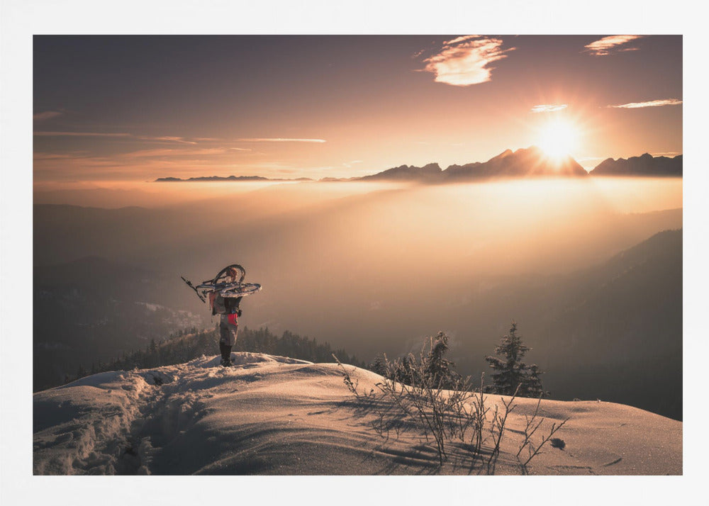 A lone person stands on a snowy mountain peak at sunrise, carrying a bicycle over their shoulder. They look out over a valley filled with a sea of clouds, with distant mountain ranges silhouetted against the bright, golden sun. Artwork