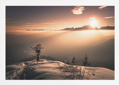 A lone person stands on a snowy mountain peak at sunrise, carrying a bicycle over their shoulder. They look out over a valley filled with a sea of clouds, with distant mountain ranges silhouetted against the bright, golden sun. Artwork