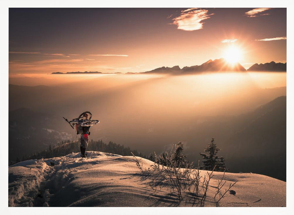 A lone person stands on a snowy mountain peak at sunrise, carrying a bicycle over their shoulder. They look out over a valley filled with a sea of clouds, with distant mountain ranges silhouetted against the bright, golden sun. Artwork