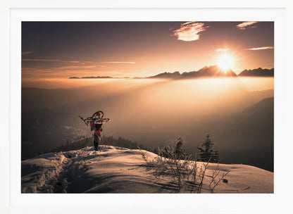 A lone person stands on a snowy mountain peak at sunrise, carrying a bicycle over their shoulder. They look out over a valley filled with a sea of clouds, with distant mountain ranges silhouetted against the bright, golden sun. Artwork