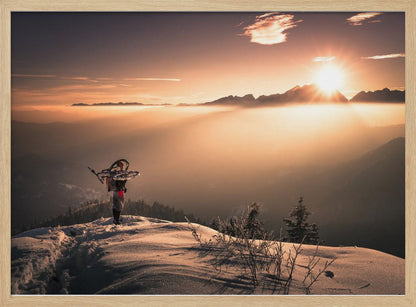A lone person stands on a snowy mountain peak at sunrise, carrying a bicycle over their shoulder. They look out over a valley filled with a sea of clouds, with distant mountain ranges silhouetted against the bright, golden sun. Artwork