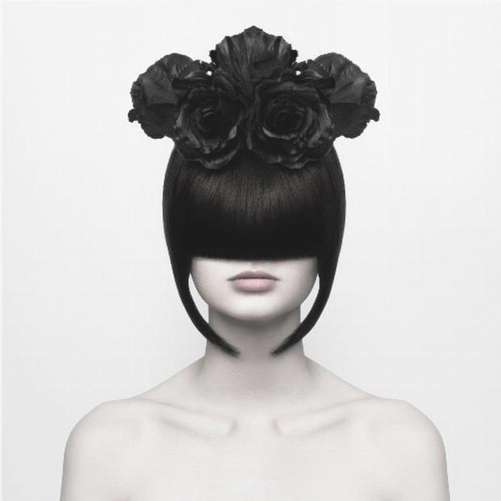 A stylized black and white portrait of a woman with a sleek black bob hairstyle where the bangs completely cover her eyes. She wears a large, elaborate headpiece made of black roses. Her expression is neutral, showing only her mouth and chin. The image is set against a plain white background and enclosed in a light wood frame. Print