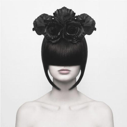 A stylized black and white portrait of a woman with a sleek black bob hairstyle where the bangs completely cover her eyes. She wears a large, elaborate headpiece made of black roses. Her expression is neutral, showing only her mouth and chin. The image is set against a plain white background and enclosed in a light wood frame. Print