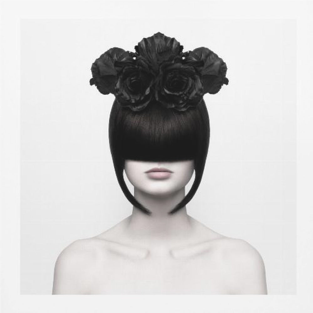 A stylized black and white portrait of a woman with a sleek black bob hairstyle where the bangs completely cover her eyes. She wears a large, elaborate headpiece made of black roses. Her expression is neutral, showing only her mouth and chin. The image is set against a plain white background and enclosed in a light wood frame. Print