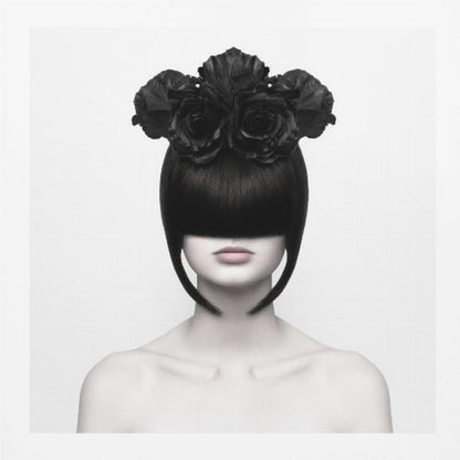 A stylized black and white portrait of a woman with a sleek black bob hairstyle where the bangs completely cover her eyes. She wears a large, elaborate headpiece made of black roses. Her expression is neutral, showing only her mouth and chin. The image is set against a plain white background and enclosed in a light wood frame. Print
