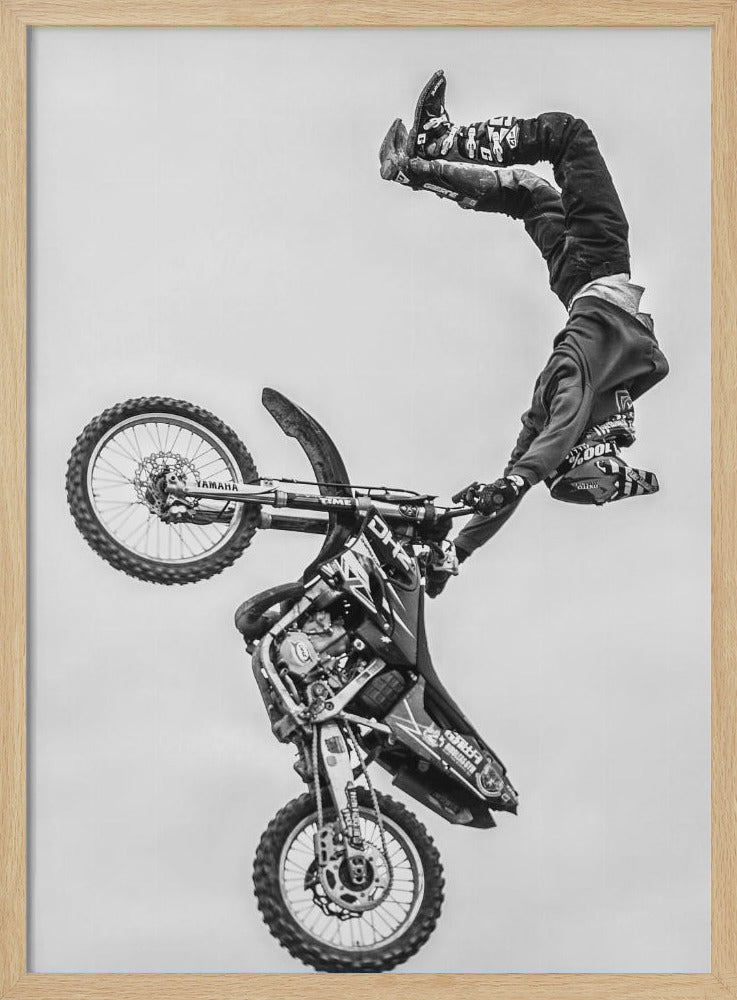 A dynamic black and white action shot of a freestyle motocross rider performing a handstand on the handlebars of their dirt bike mid-air. The bike is nearly vertical against a plain white sky, capturing a moment of extreme athleticism and balance. Poster