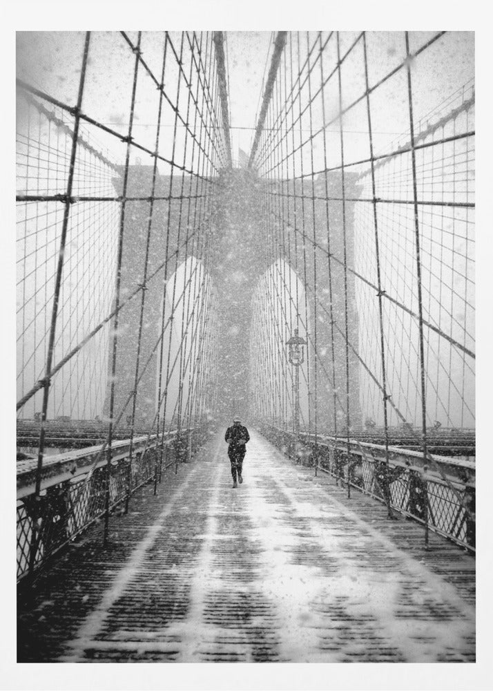 A vertical, black and white photograph of a solitary person walking along the Brooklyn Bridge during a heavy snowstorm. The iconic cables and towers of the bridge create a strong sense of perspective, drawing the eye towards the distant, hazy towers while snow falls all around. Artwork