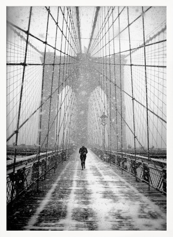A vertical, black and white photograph of a solitary person walking along the Brooklyn Bridge during a heavy snowstorm. The iconic cables and towers of the bridge create a strong sense of perspective, drawing the eye towards the distant, hazy towers while snow falls all around. Artwork
