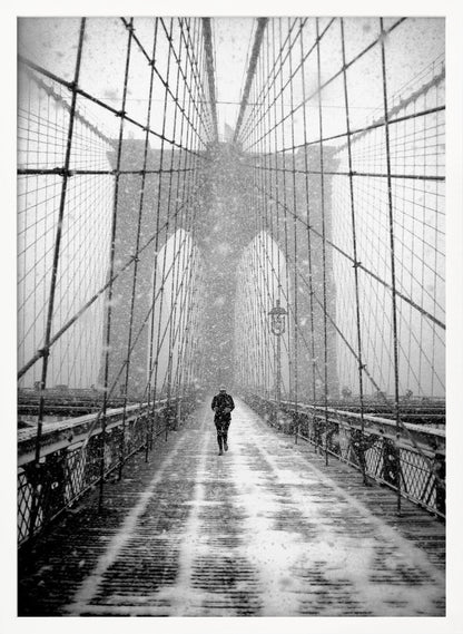 A vertical, black and white photograph of a solitary person walking along the Brooklyn Bridge during a heavy snowstorm. The iconic cables and towers of the bridge create a strong sense of perspective, drawing the eye towards the distant, hazy towers while snow falls all around. Artwork