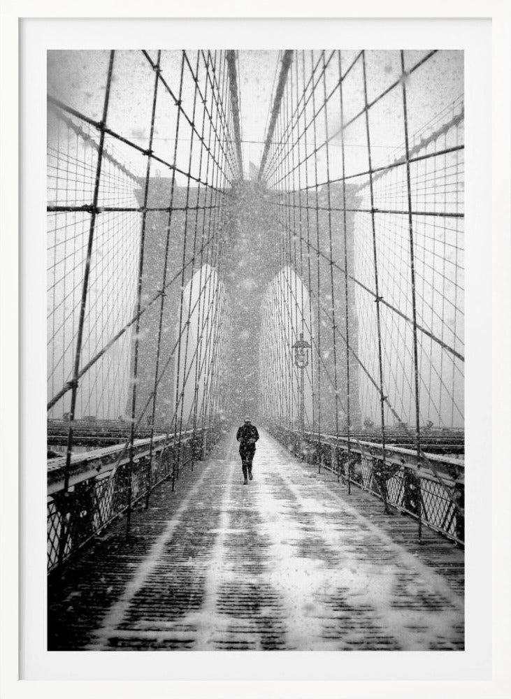 A vertical, black and white photograph of a solitary person walking along the Brooklyn Bridge during a heavy snowstorm. The iconic cables and towers of the bridge create a strong sense of perspective, drawing the eye towards the distant, hazy towers while snow falls all around. Artwork
