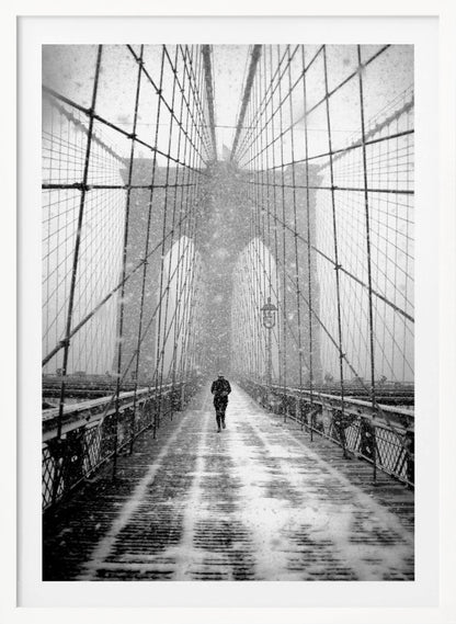 A vertical, black and white photograph of a solitary person walking along the Brooklyn Bridge during a heavy snowstorm. The iconic cables and towers of the bridge create a strong sense of perspective, drawing the eye towards the distant, hazy towers while snow falls all around. Artwork