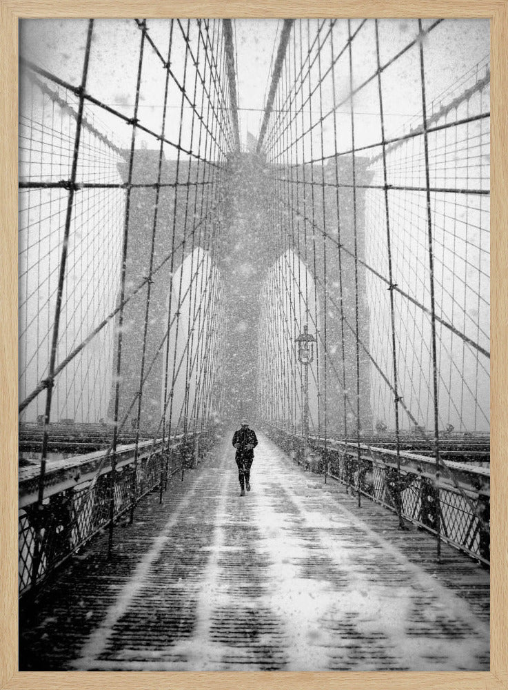 A vertical, black and white photograph of a solitary person walking along the Brooklyn Bridge during a heavy snowstorm. The iconic cables and towers of the bridge create a strong sense of perspective, drawing the eye towards the distant, hazy towers while snow falls all around. Artwork