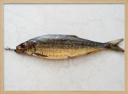 A surreal photograph of a whole smoked fish with a cigarette butt in its mouth, laying horizontally on a white marble surface, all within a silver frame. Wall Art