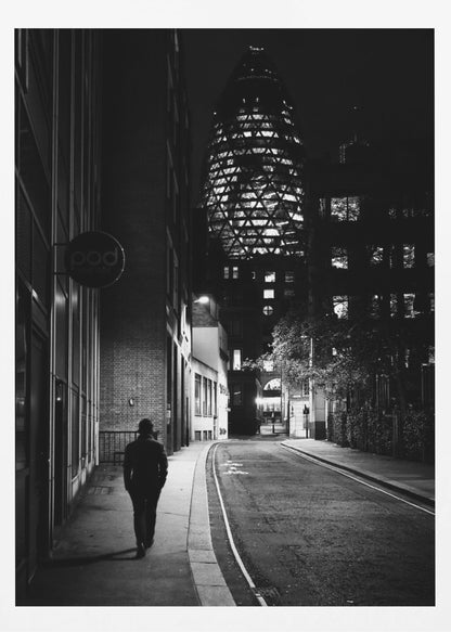 A moody black and white photograph of a person walking away down a narrow, deserted city street at night. In the background, the iconic Gherkin building in London is brightly lit against the dark sky. Wall Art