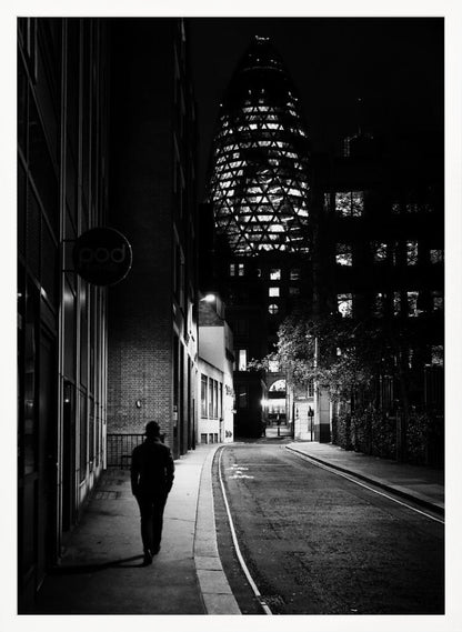 A moody black and white photograph of a person walking away down a narrow, deserted city street at night. In the background, the iconic Gherkin building in London is brightly lit against the dark sky. Wall Art