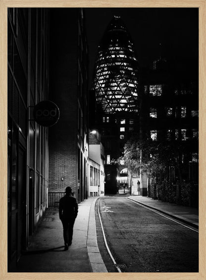 A moody black and white photograph of a person walking away down a narrow, deserted city street at night. In the background, the iconic Gherkin building in London is brightly lit against the dark sky. Wall Art