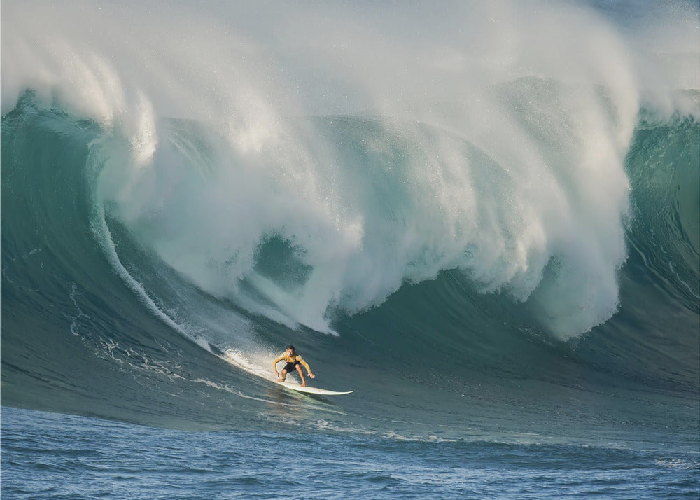 A lone surfer in a yellow shirt rides down the face of an enormous, powerful ocean wave as it crests into white foam, viewed within a silver picture frame. Wall Art