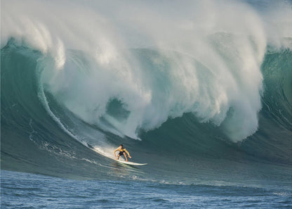 A lone surfer in a yellow shirt rides down the face of an enormous, powerful ocean wave as it crests into white foam, viewed within a silver picture frame. Wall Art