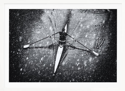 A dramatic black and white overhead photograph of a single rower in a narrow scull, captured mid-stroke as they cut through dark water during a heavy snowfall, creating a high-contrast and atmospheric scene. Decor