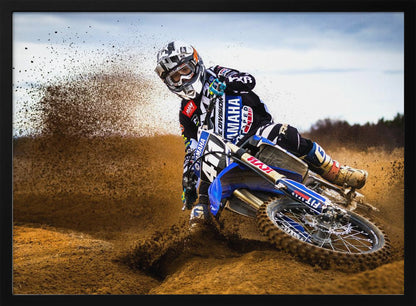 A motocross rider in full gear leans sharply into a turn on a dirt track, kicking up a large spray of mud and dirt from their blue and white Yamaha motorcycle. Artwork