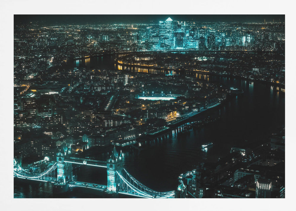 A framed aerial photograph of London at night, featuring the iconic Tower Bridge illuminated in bright teal in the foreground and the glowing skyscrapers of Canary Wharf across the River Thames in the background. Artwork