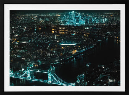 A framed aerial photograph of London at night, featuring the iconic Tower Bridge illuminated in bright teal in the foreground and the glowing skyscrapers of Canary Wharf across the River Thames in the background. Artwork