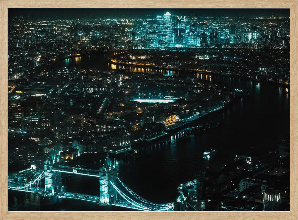 A framed aerial photograph of London at night, featuring the iconic Tower Bridge illuminated in bright teal in the foreground and the glowing skyscrapers of Canary Wharf across the River Thames in the background. Artwork
