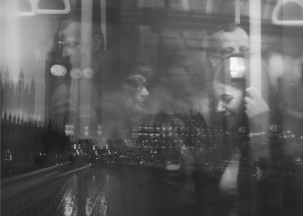 A moody black and white double exposure photograph showing a rainy London street at night with Big Ben, overlaid with the faint reflections of people inside a moving vehicle like a bus. The image has a dreamy, layered effect and is displayed in a silver frame. Print