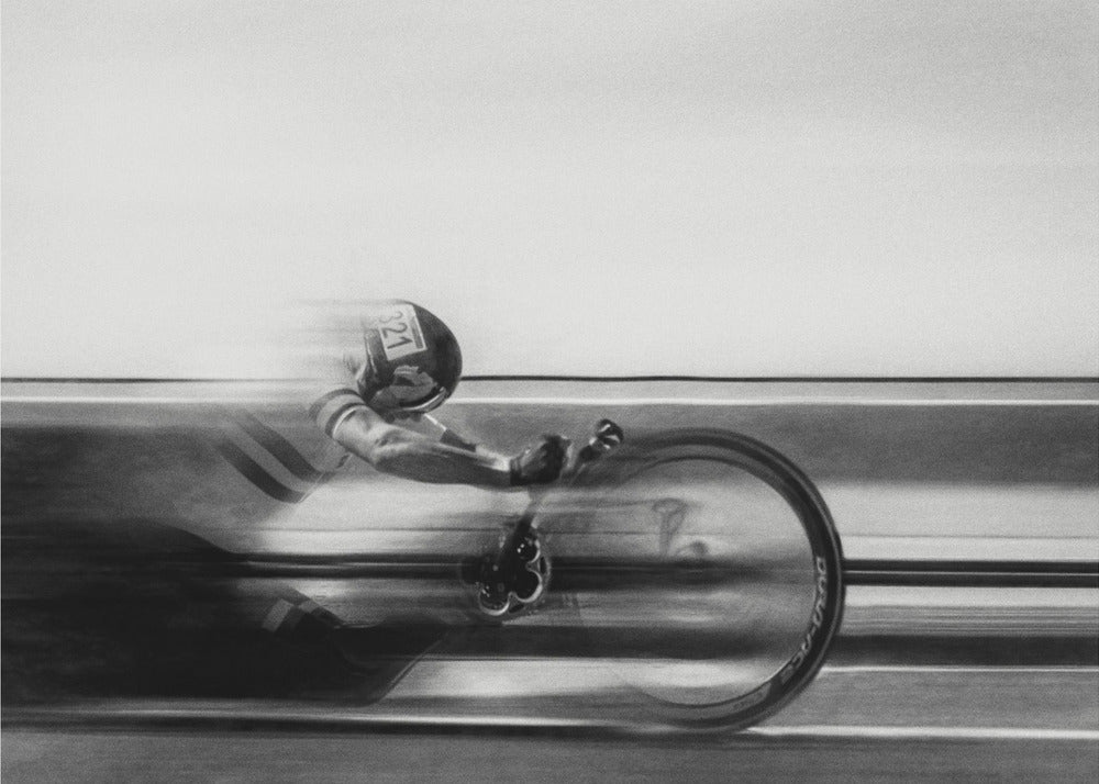 A black and white photograph captured with motion blur, showing a cyclist in an aerodynamic position racing at high speed. The background is blurred into horizontal lines, emphasizing the velocity. The image is enclosed in a silver frame. Wall Art