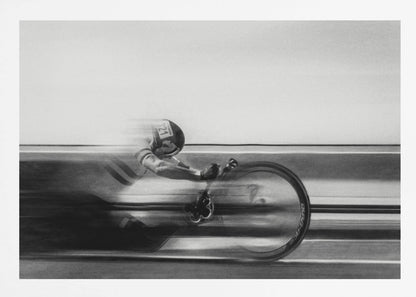A black and white photograph captured with motion blur, showing a cyclist in an aerodynamic position racing at high speed. The background is blurred into horizontal lines, emphasizing the velocity. The image is enclosed in a silver frame. Wall Art