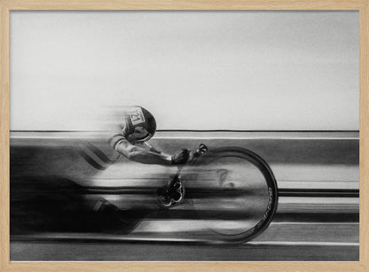A black and white photograph captured with motion blur, showing a cyclist in an aerodynamic position racing at high speed. The background is blurred into horizontal lines, emphasizing the velocity. The image is enclosed in a silver frame. Wall Art