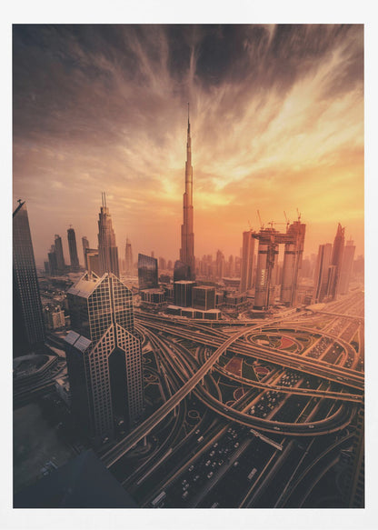 A dramatic high-angle photograph of the Dubai skyline at sunset. The Burj Khalifa stands tall in the center, bathed in the warm light of the setting sun, while a complex network of highways and interchanges weaves between modern skyscrapers in the foreground under a cloudy, orange-tinted sky. Poster