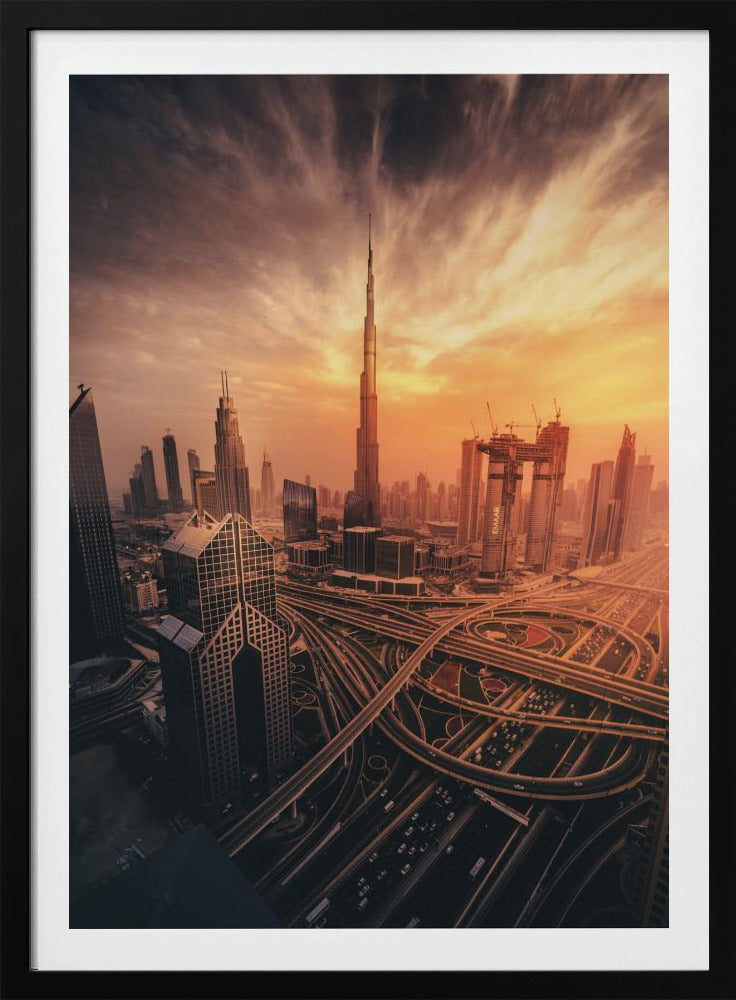 A dramatic high-angle photograph of the Dubai skyline at sunset. The Burj Khalifa stands tall in the center, bathed in the warm light of the setting sun, while a complex network of highways and interchanges weaves between modern skyscrapers in the foreground under a cloudy, orange-tinted sky. Poster